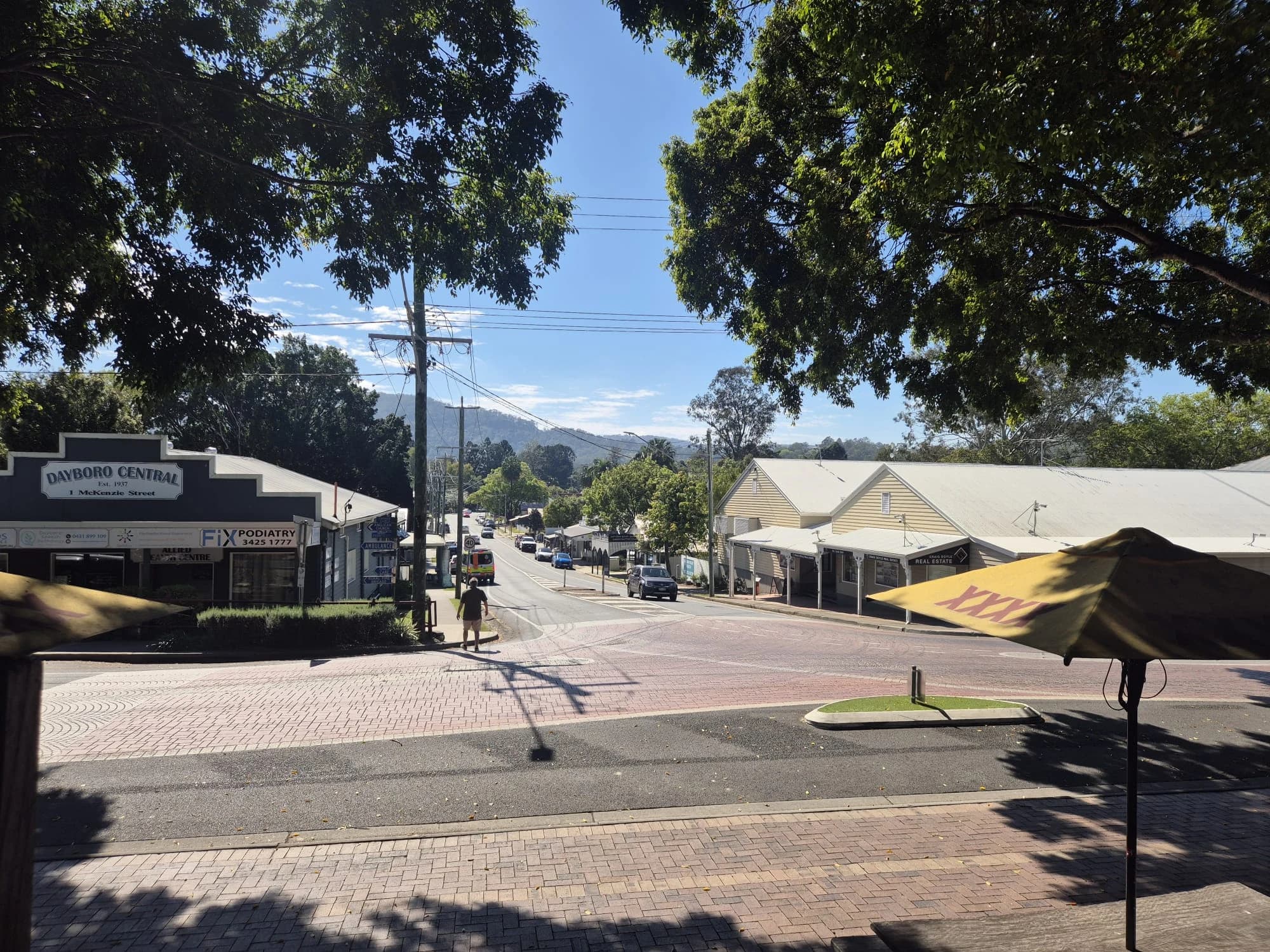 A Dayboro street viewed from a shaded pavement beneath trees.