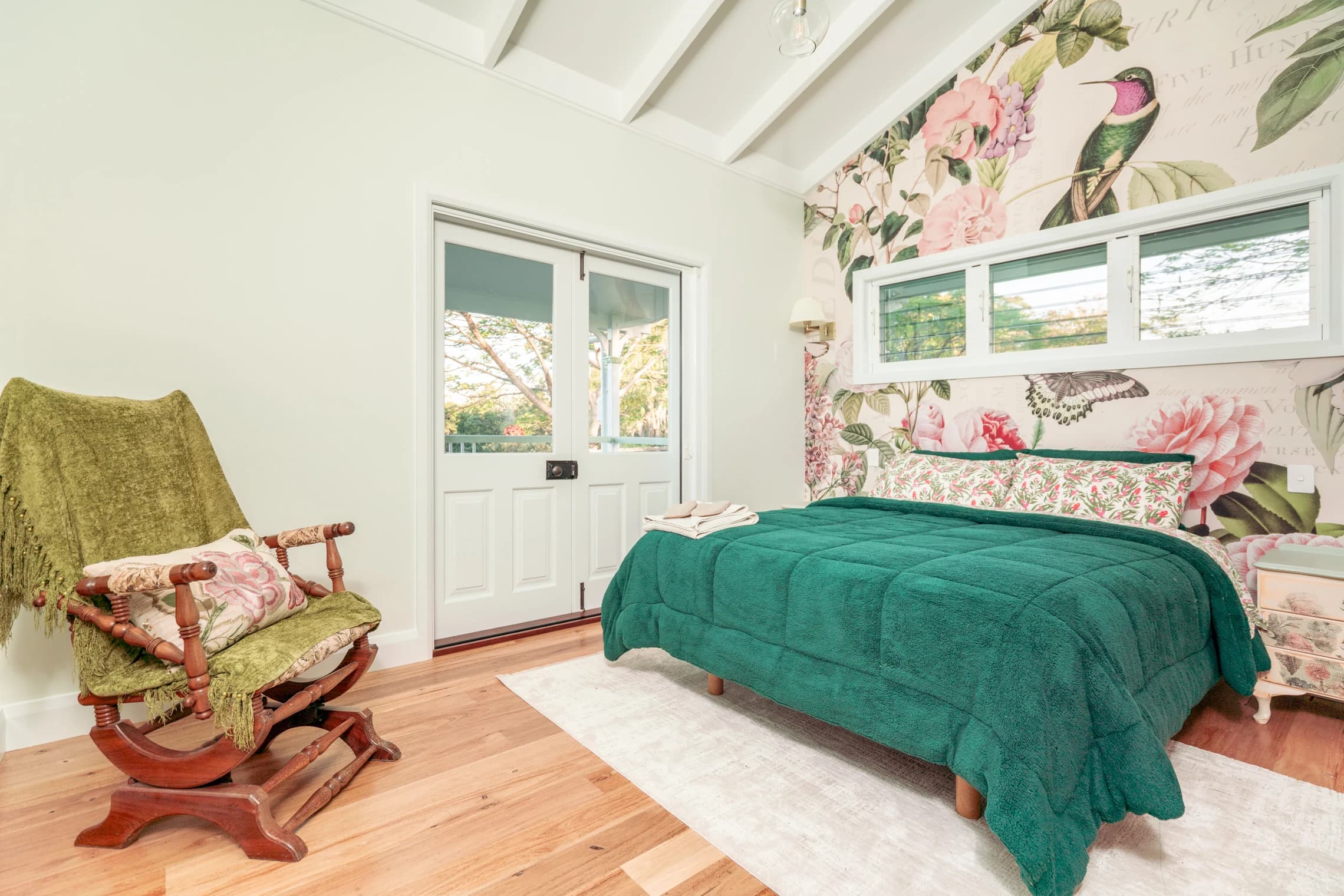 Bedroom with botanical wallpaper, a green quilt and French doors to the veranda.