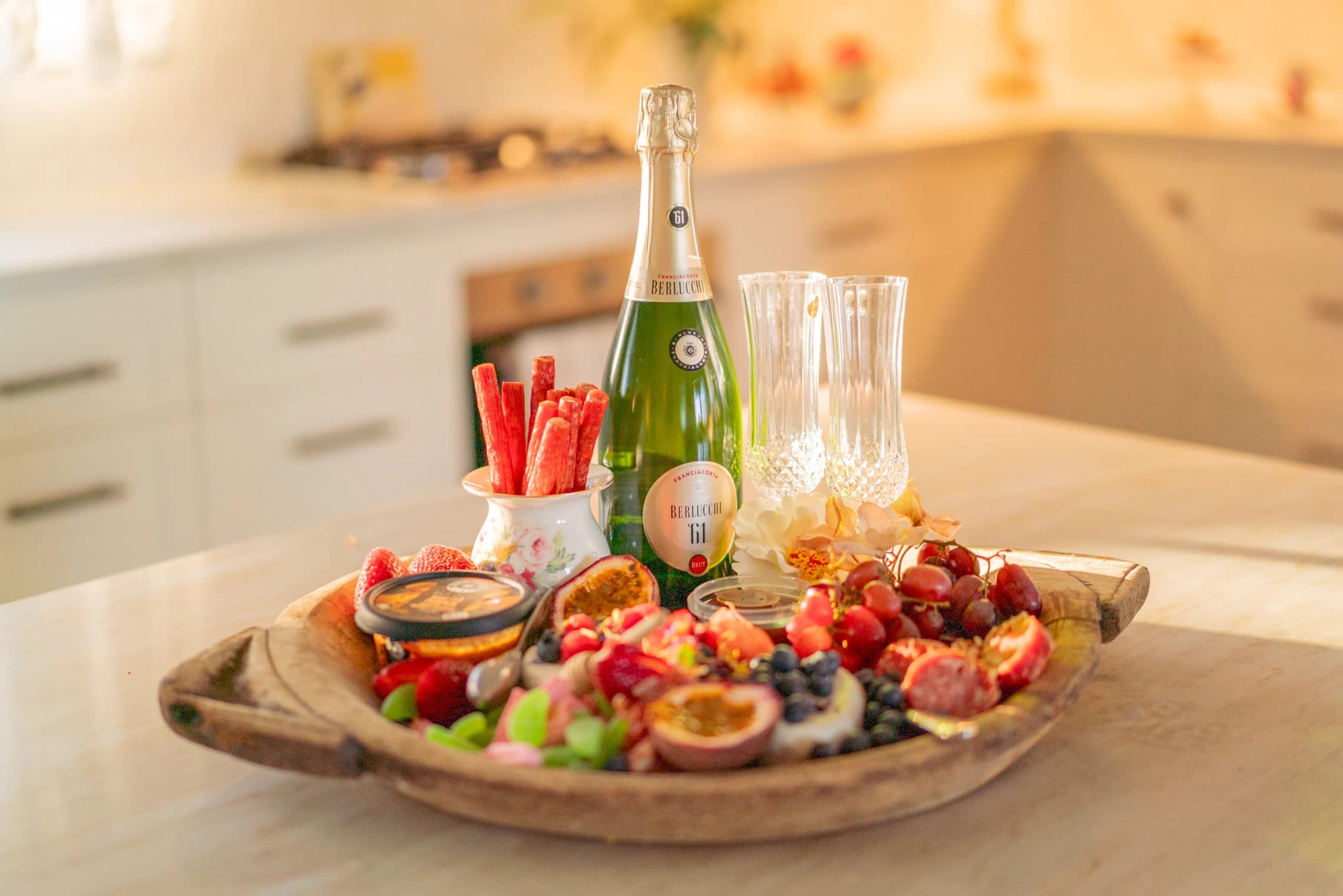 A fruit and cheese platter with sparkling wine on the kitchen island.