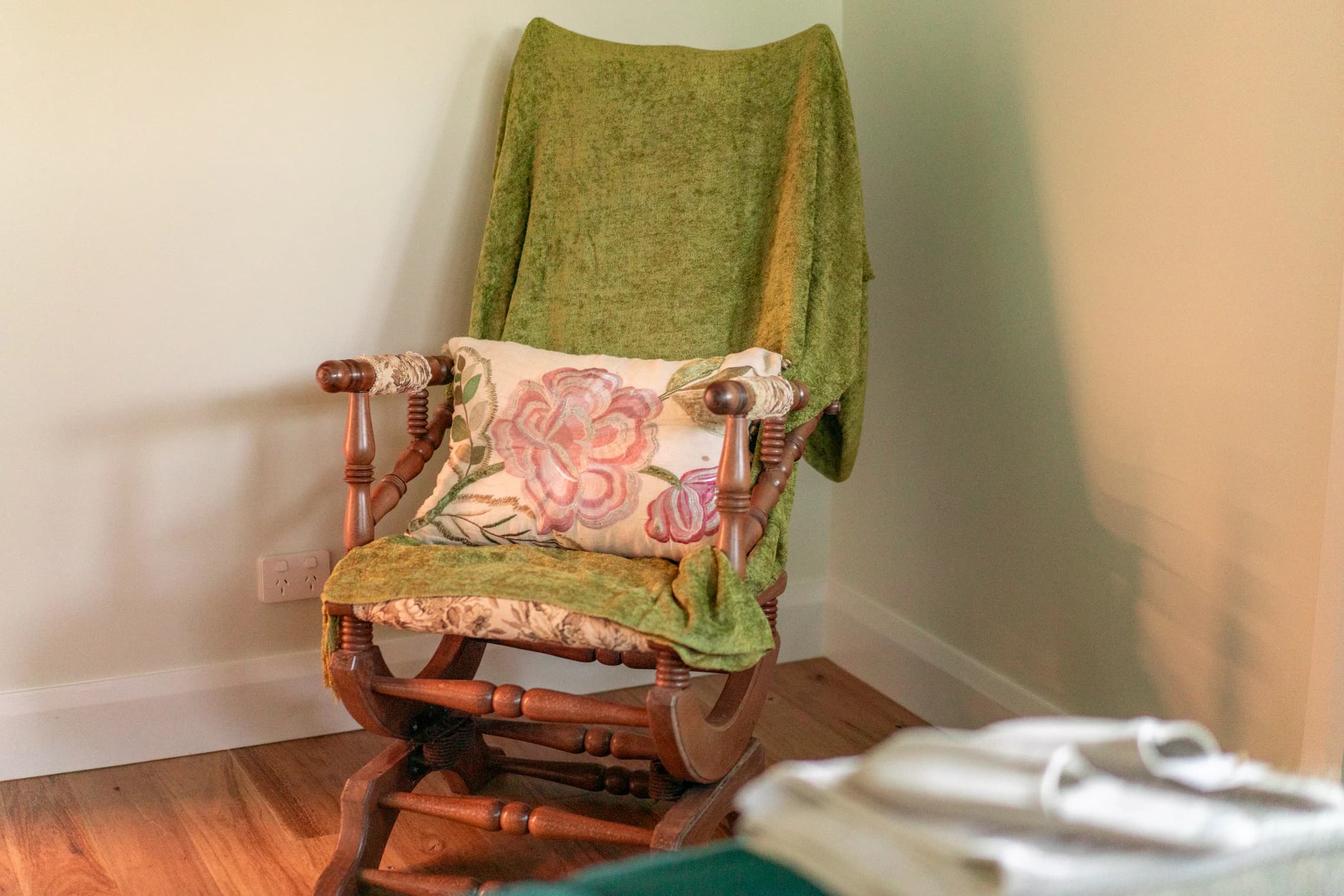 A timber rocking chair with a green throw and floral cushion.