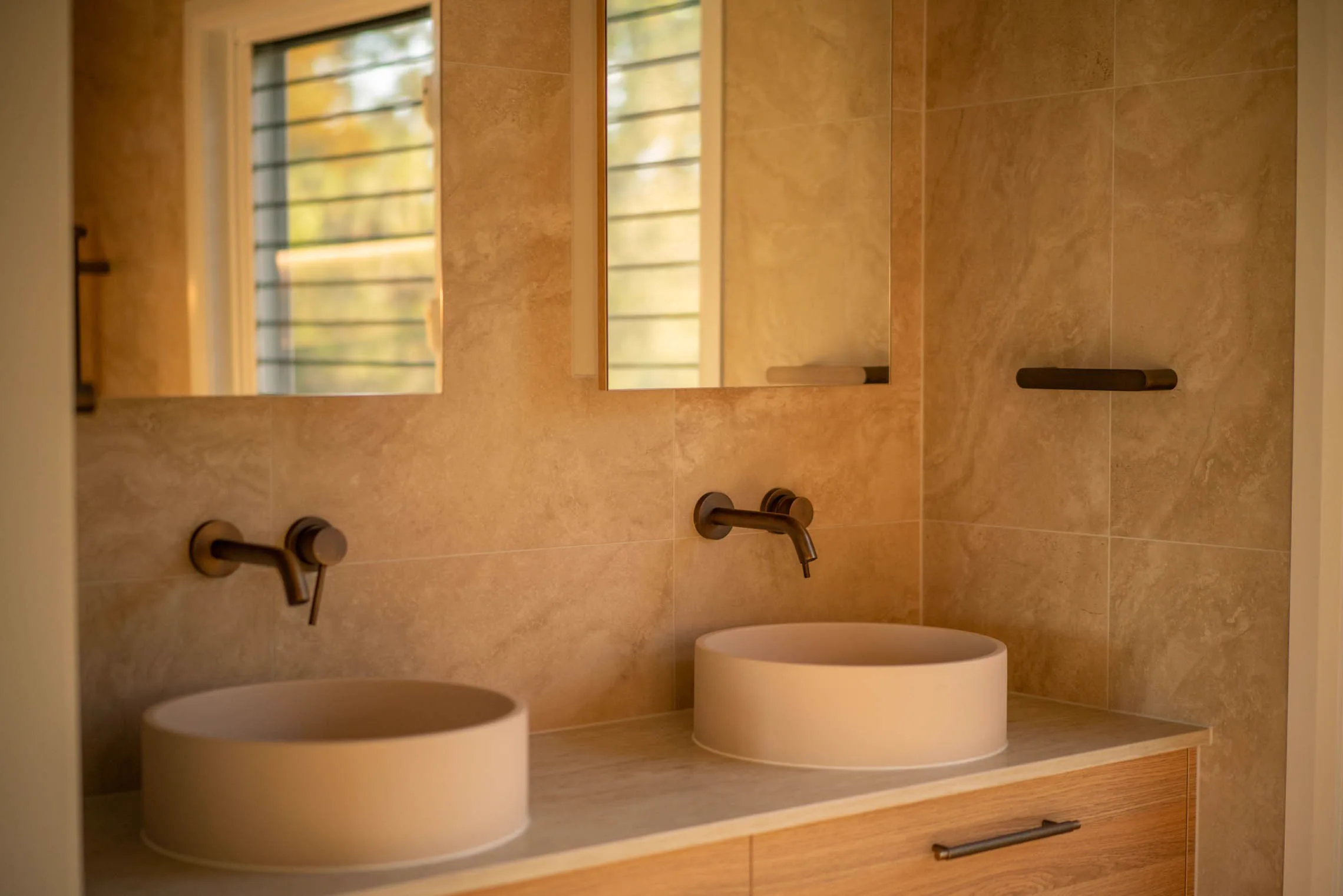 Twin stone basins and brass tapware beneath louvre windows in the ensuite.
