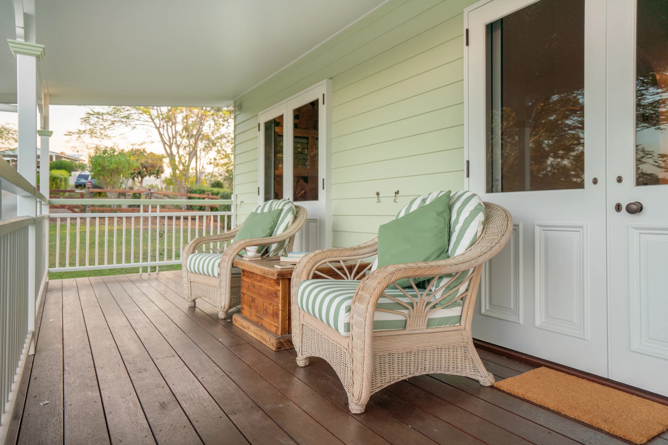 Wicker chairs with green cushions along the cottage's timber veranda.