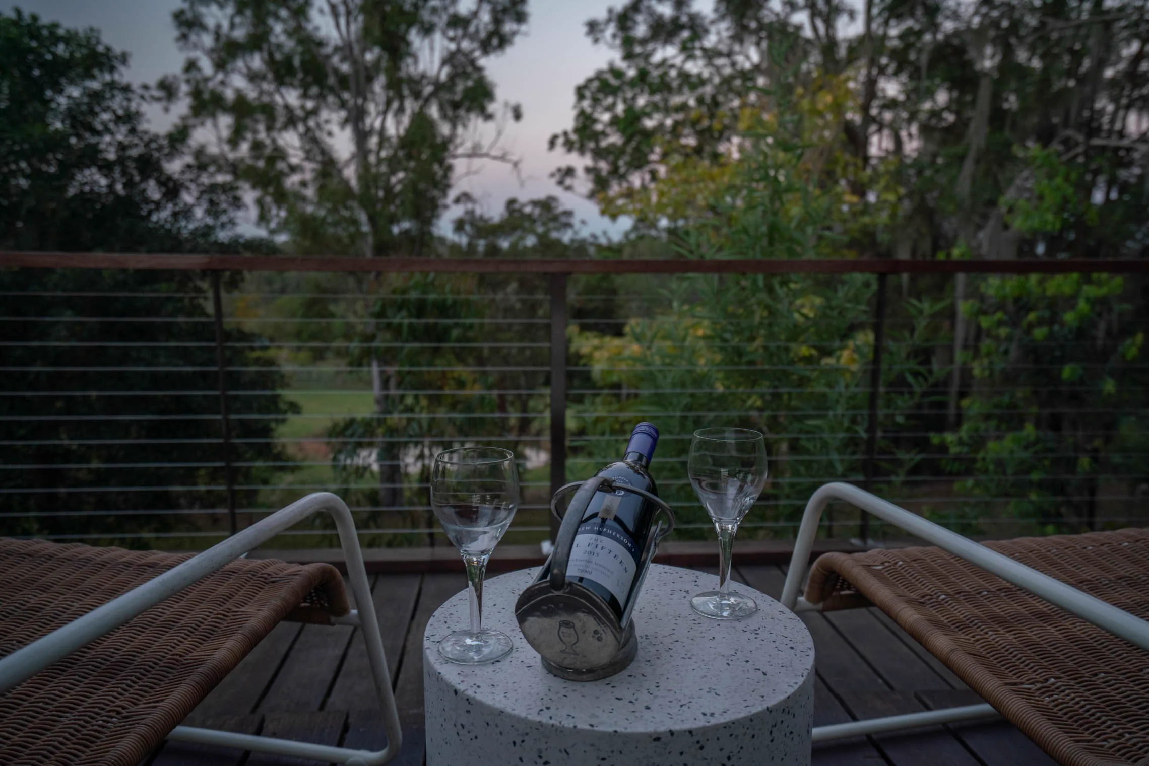 A bottle and two glasses on the deck table, looking out over the trees.