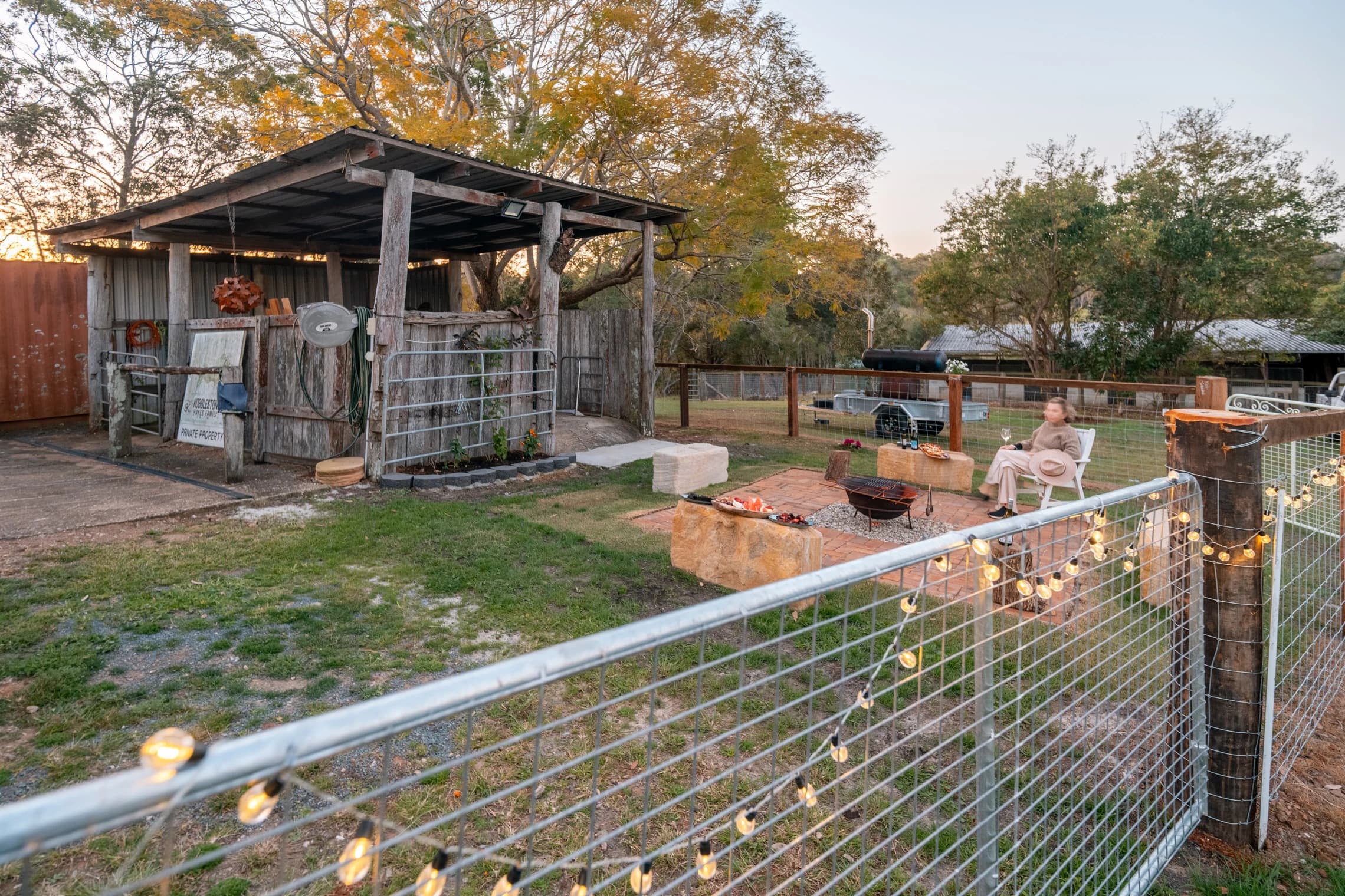 A rustic shed and outdoor fire-pit seating seen across the garden railing.