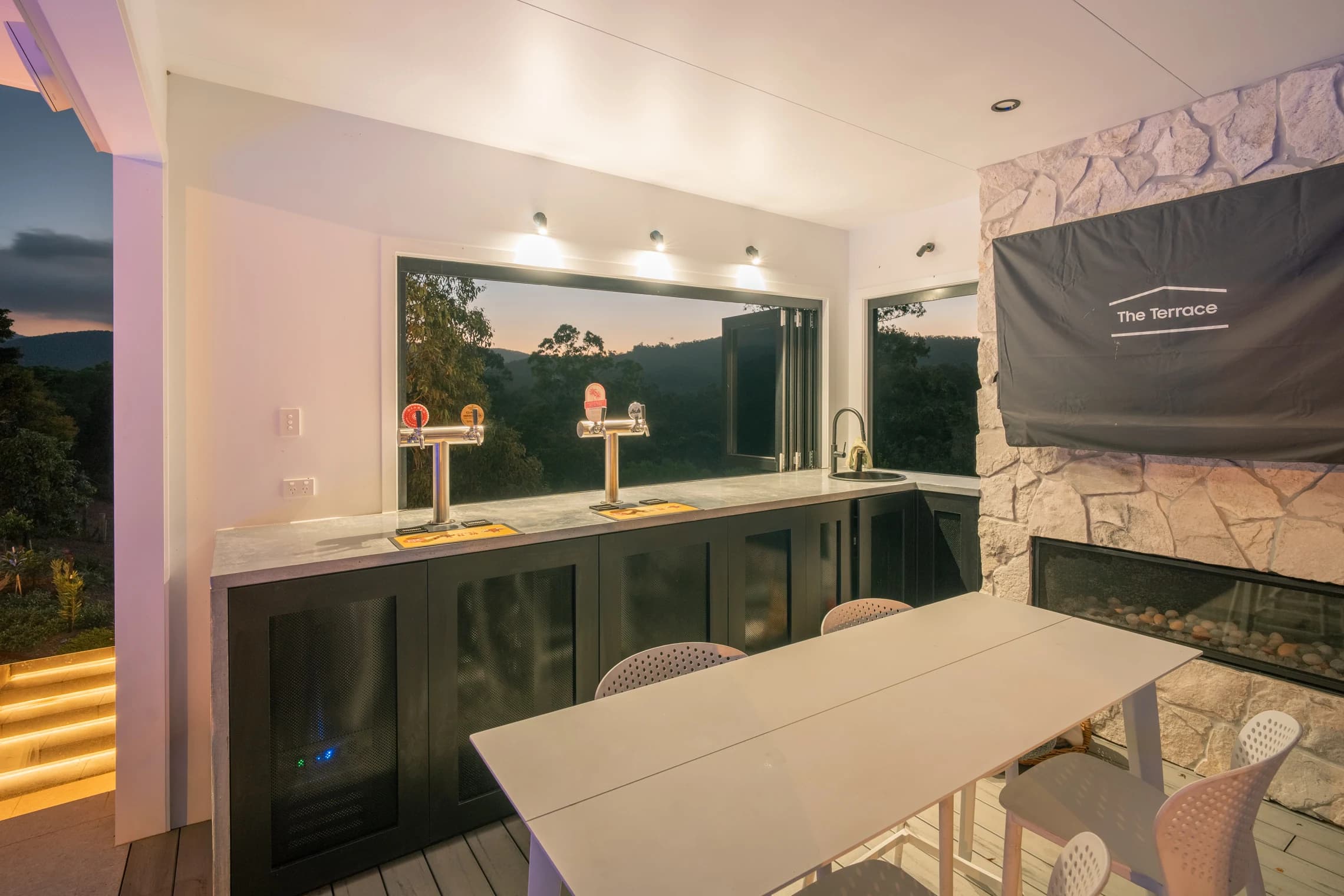 A poolside bar with taps, counter seating and an open window onto the landscape.