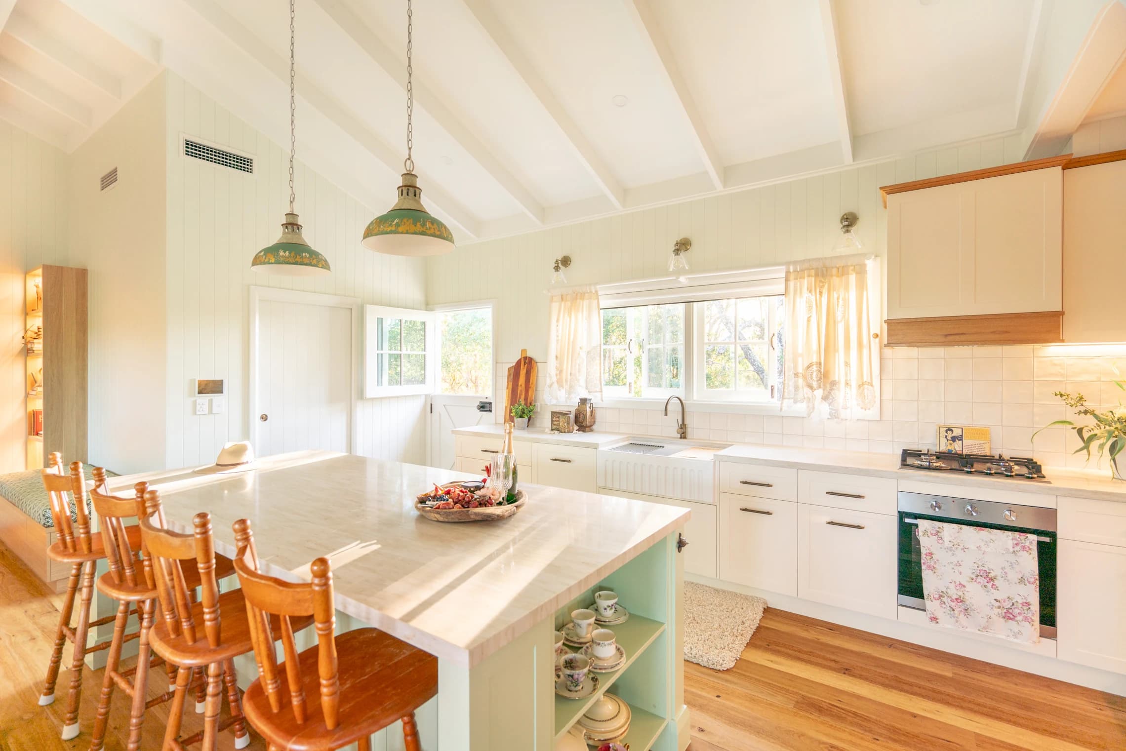 The sage kitchen island with timber stools, sink and cooktop behind.
