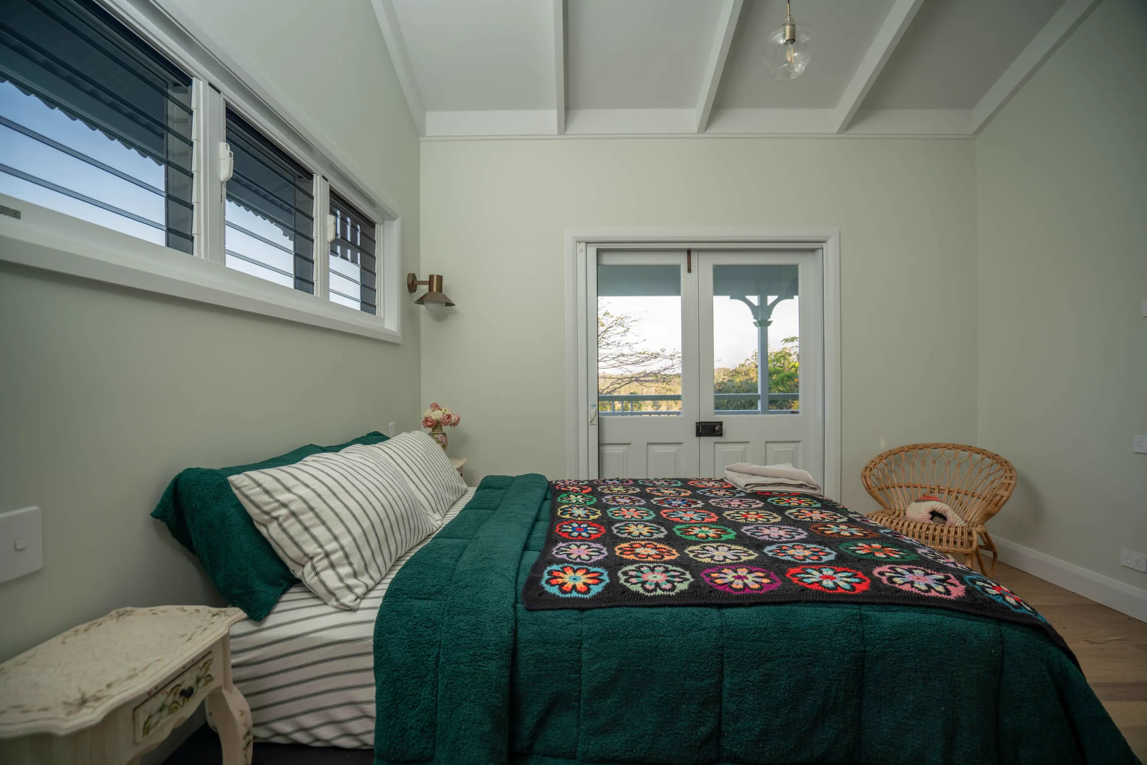 Mint bedroom with a green quilt, striped pillows and a rattan chair by the French doors.