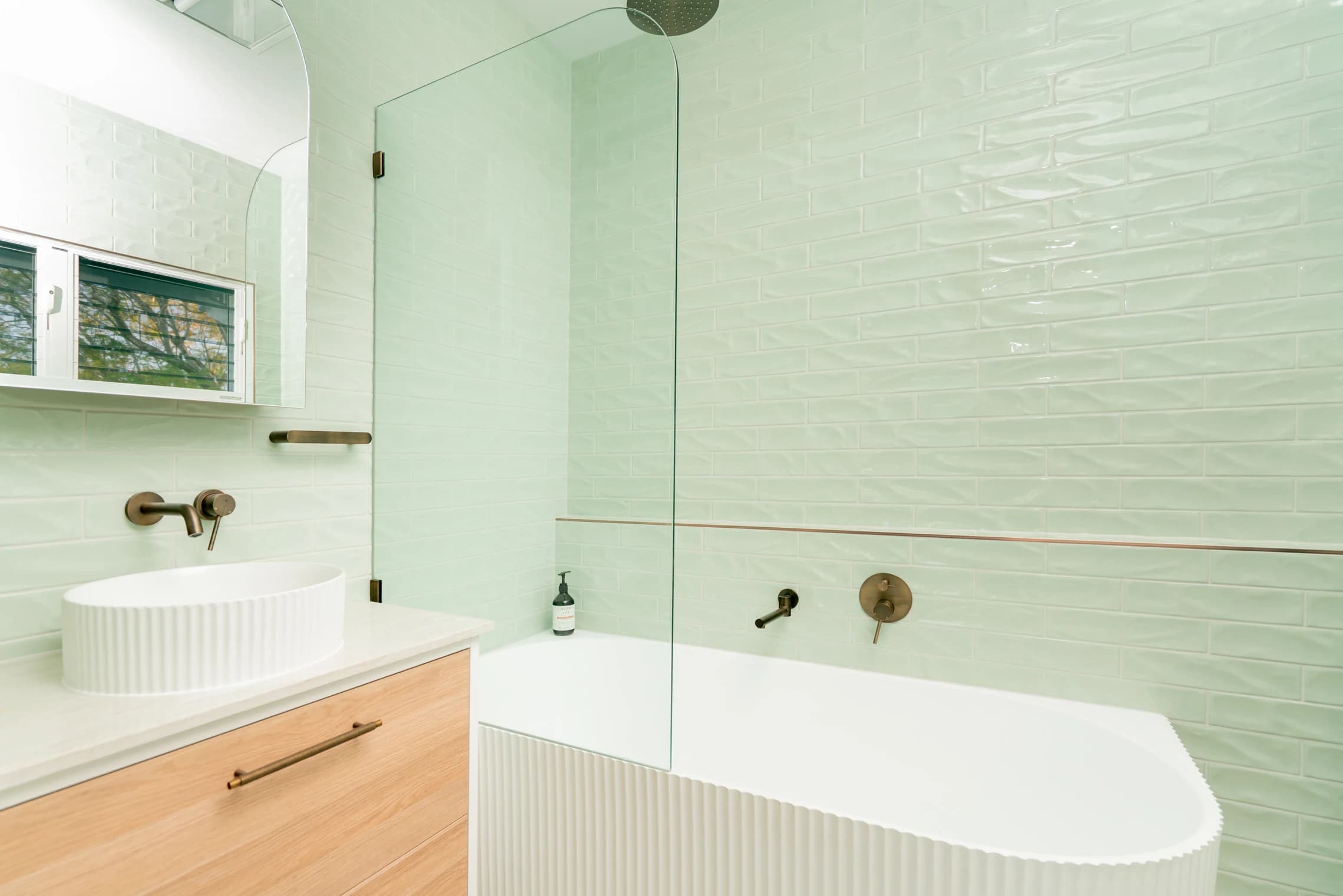 A freestanding bath and basin against mint-green tiles with brass taps.
